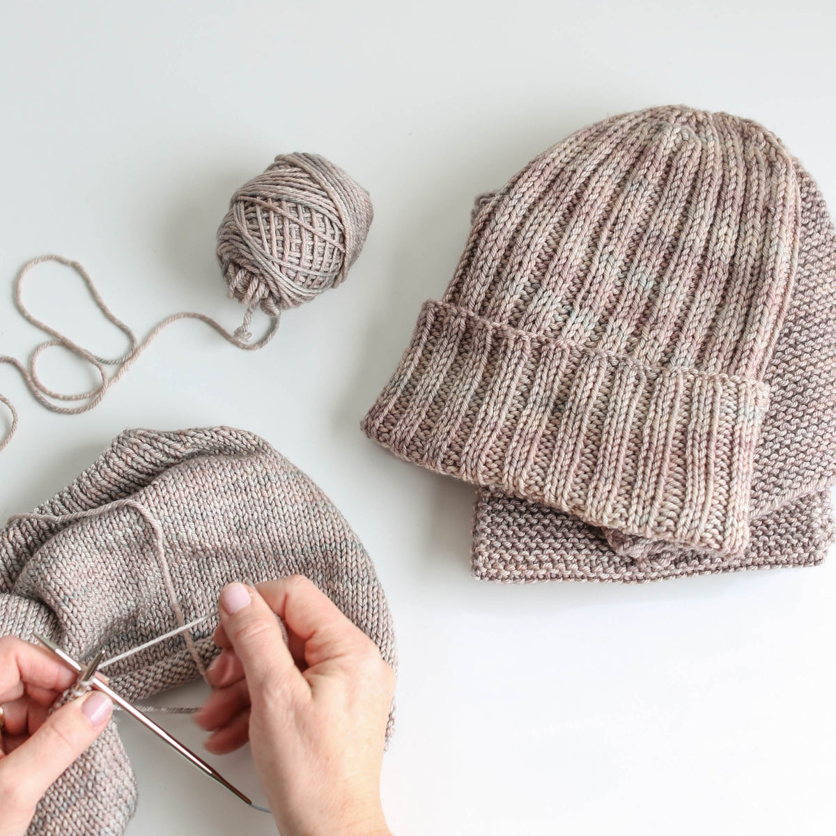 Grey rib knit beanie hat & hands working on a matching knitting project.